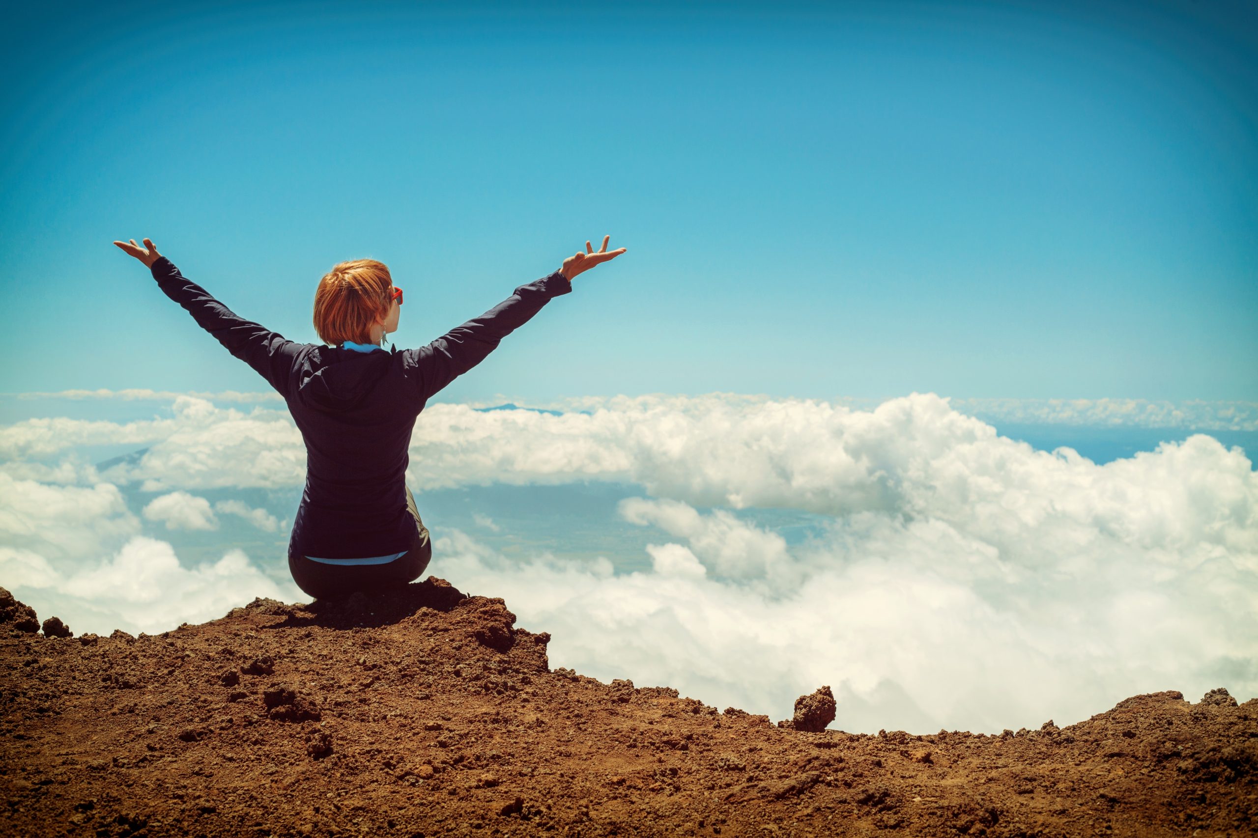 person-sitting-on-cliff-raising-up-both-